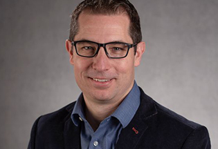 A smiling Dr. Anderson wears dark glasses, a suit jacket and blue collared shirt.